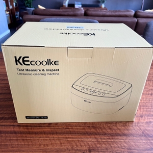 Kecoolke-SU-787B im Karton auf einem Tisch, im Hintergrund sieht man eine Wohnzimmercouch