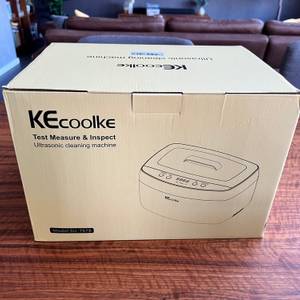 Kecoolke-SU-787B im Karton auf einem Tisch, im Hintergrund sieht man eine Wohnzimmercouch