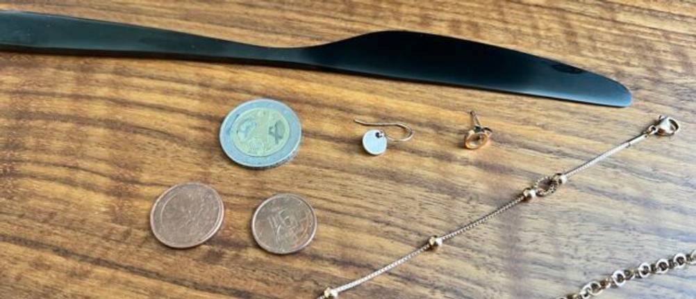 Schmuck, Münzen und schwarzes Messer auf Tisch