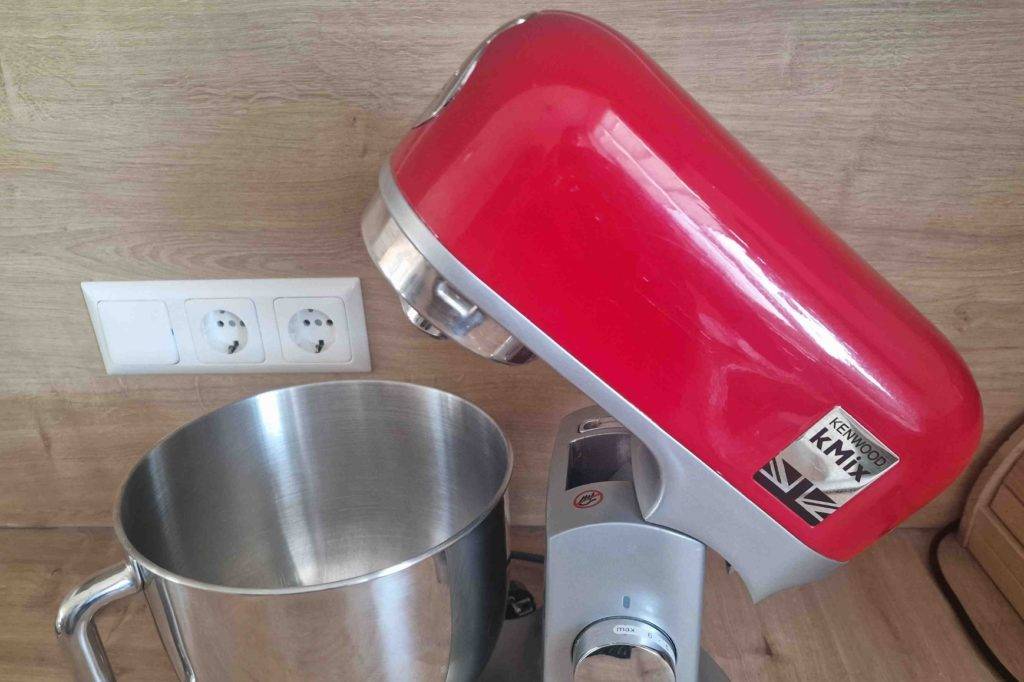 Seitliche Draufsicht einer Kenwood-Küchenmaschine im Test: Modell Kmix mit erhobenem, roten, beweglichen Rührarm und der edelstahl-Rührschüssel.