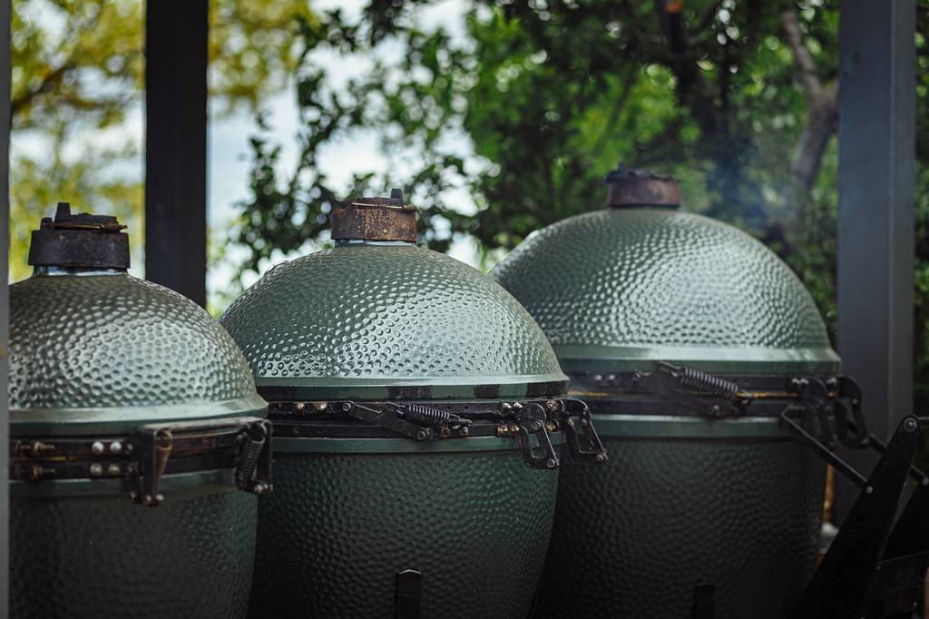 Drei grüne Keramikgrills in unterschiedlichen Größen stehen auf einer Terrasse.