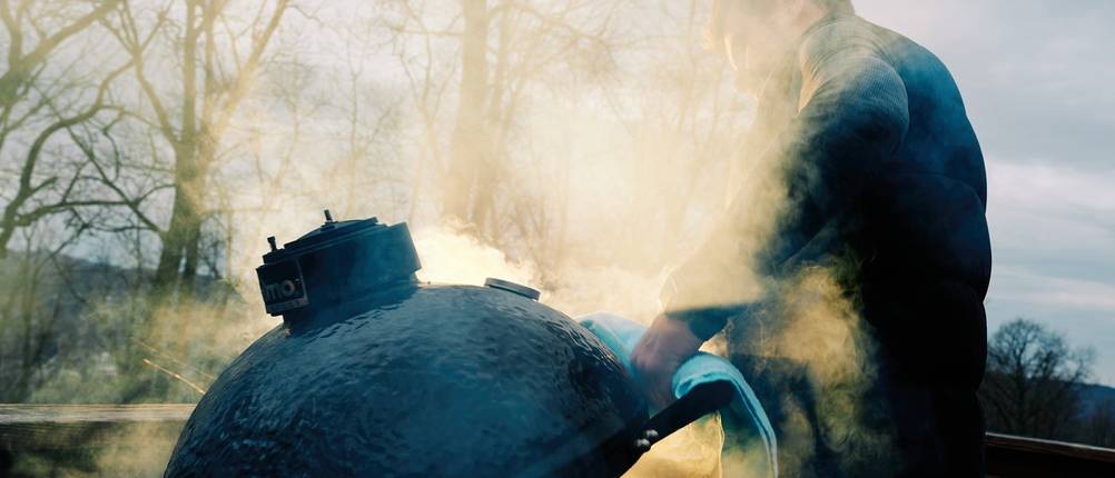 Ein Mann öffnet einen Keramikgrill im Winter.