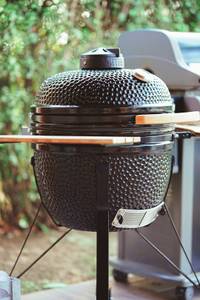 Ein schwarzer Keramikgrill mit einer hölzernen Ablagefläche steht in einem Garten.