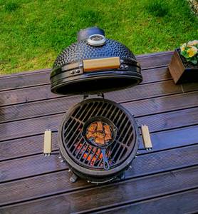 Ein schwarzer Keramikgrill mit gusseisernem Grillrost steht auf einer Terrasse.