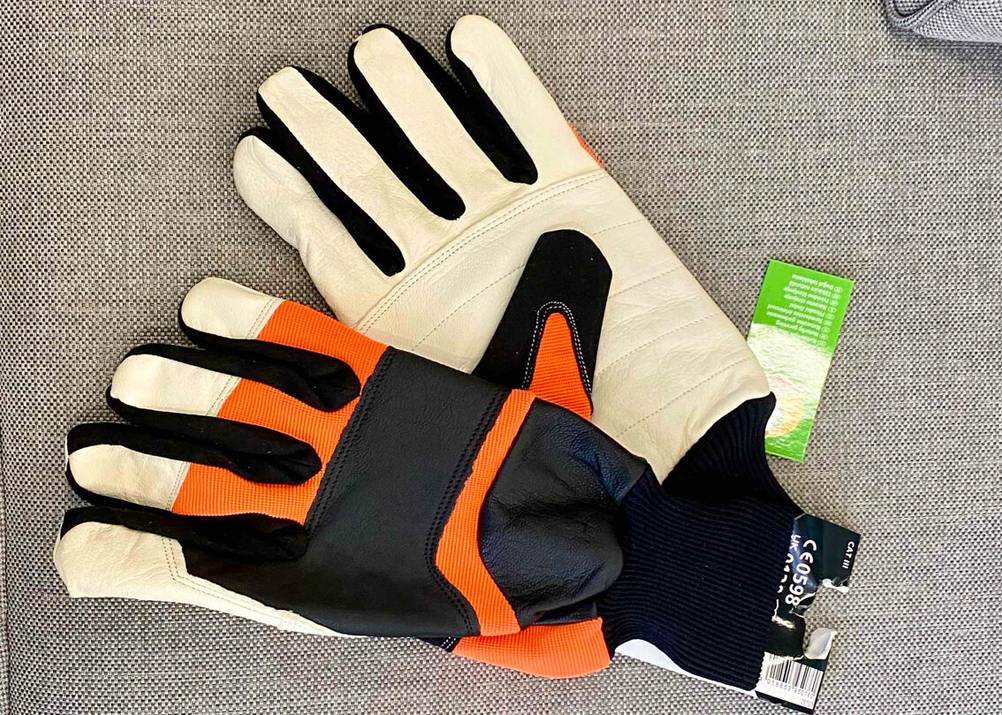 Ein Paar Arbeitshandschuhe im Test in Orange-weiß-schwarz liegen auf einem hellgrauen Sitzkissen.