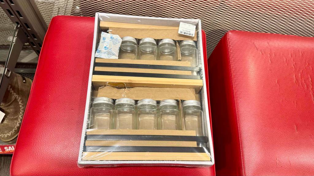 Gewürzregal-Test: Ein Holzregal mit leeren Gewürzdosen aus Glas liegt eingepackt auf einem roten Hocker.