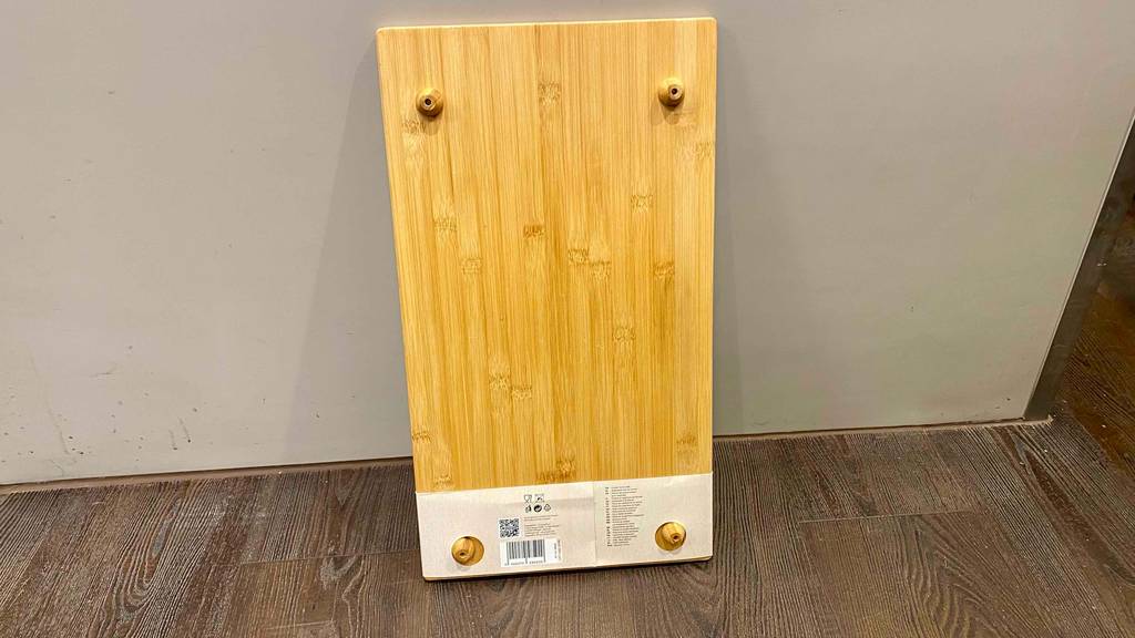 Im Test: Eine Herdabdeckplatte aus Holz inklusive runder Standfüße lehnt an einer Wand.