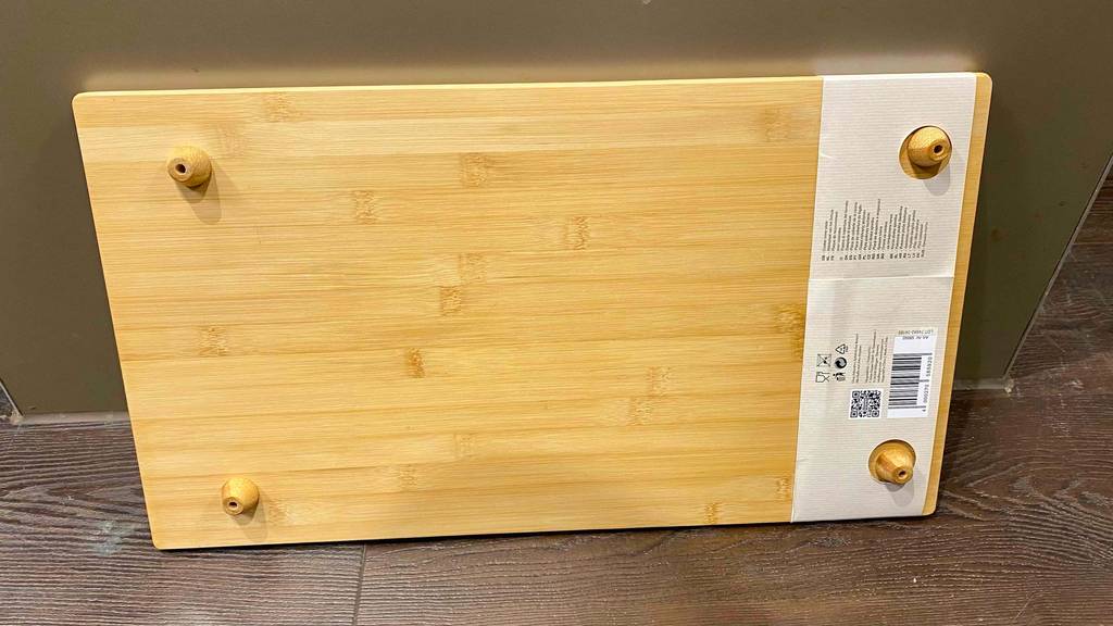 Nahansicht der Rückseite inklusive Holz-Standfüßen einer Herdabdeckplatte im Test, die aus Holz besteht und an einer braunen Fläche lehnt.