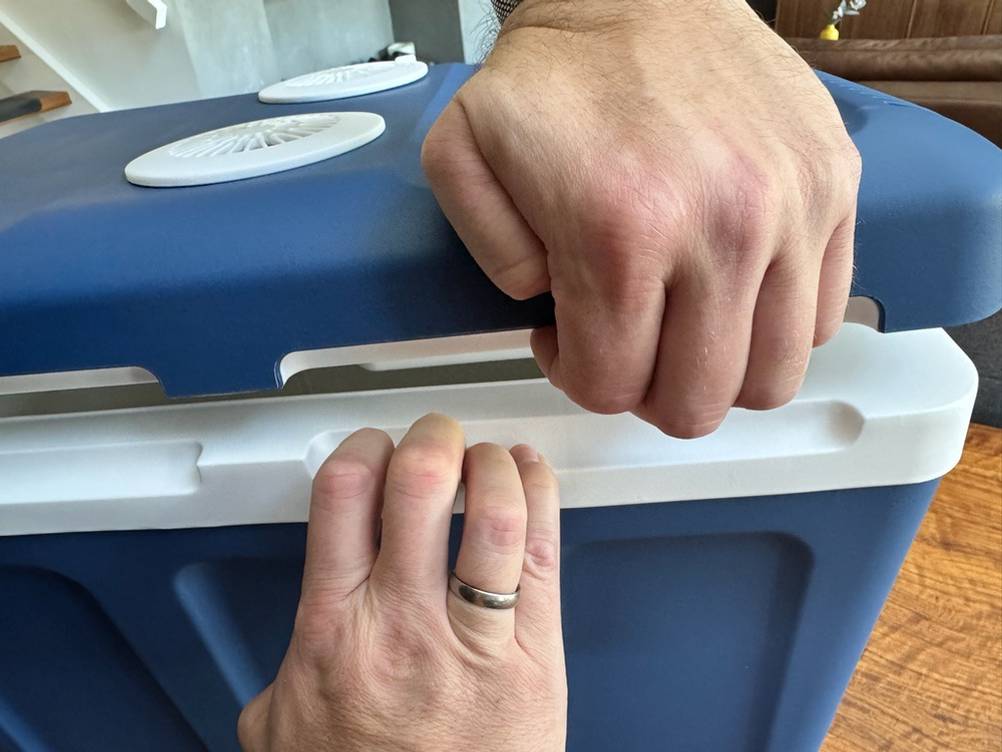Zwei Hände öffnen den Deckel der Kesser-Kühlbox mit Rädern.