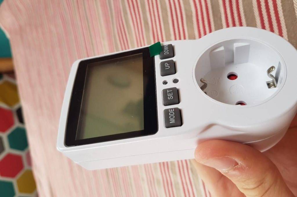 Hand hält ein getestetes Energiemessgerät der Marke Ketotek vor einen weiß-rot gesteiften Stoff.