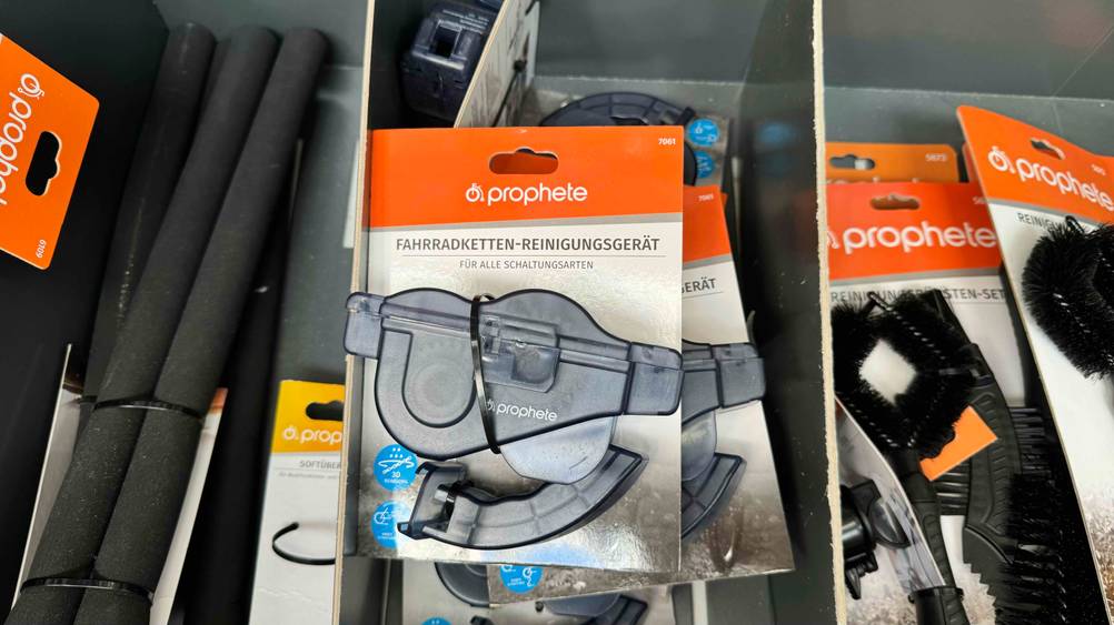 Ein getestetes Kettenreinigungsgerät in Verpackung in einem Verkaufsregal mit anderen Produkten liegend.