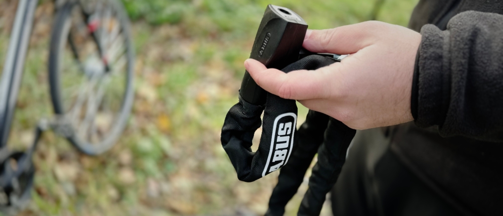 Das geöffnete Kettenschloss von Abus mit Schlüssel wird in der Hand gehalten.