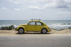 Oldtimer-Versicherungen getestet: Gelber Käfer steht seitlich einer Straße am Strand.