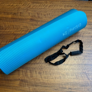 Die Kg-Physio-Yogamatte liegt neben ihrem Tragegurt auf einem Tisch