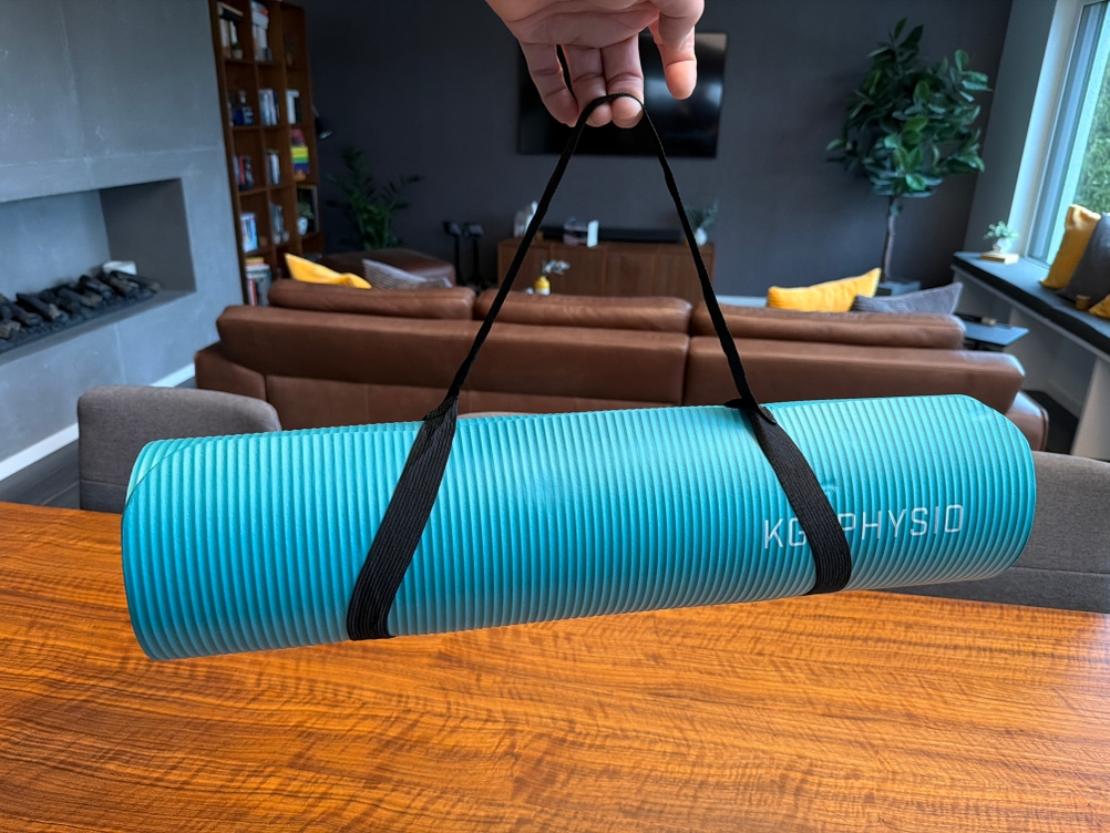 Eine Hand hält die Kg-Physio-Yogamatte am Tragegurt hoch