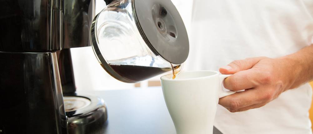 KHG-Kaffeemaschine-Test: Ein Mann gießt sich Kaffee aus einer Glaskanne in eine Tasse ein. 