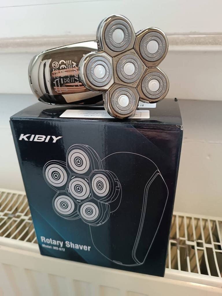 Kopfrasierer im Test der Marke Kiby mit sechs Scherköpfen im Edelstahldesign liegt auf seiner blauen Originalverpackung.