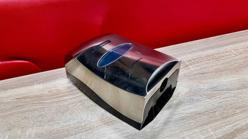 Ein Desinfektionsspender mit Sensor liegt getestet auf einem Holzbrett.