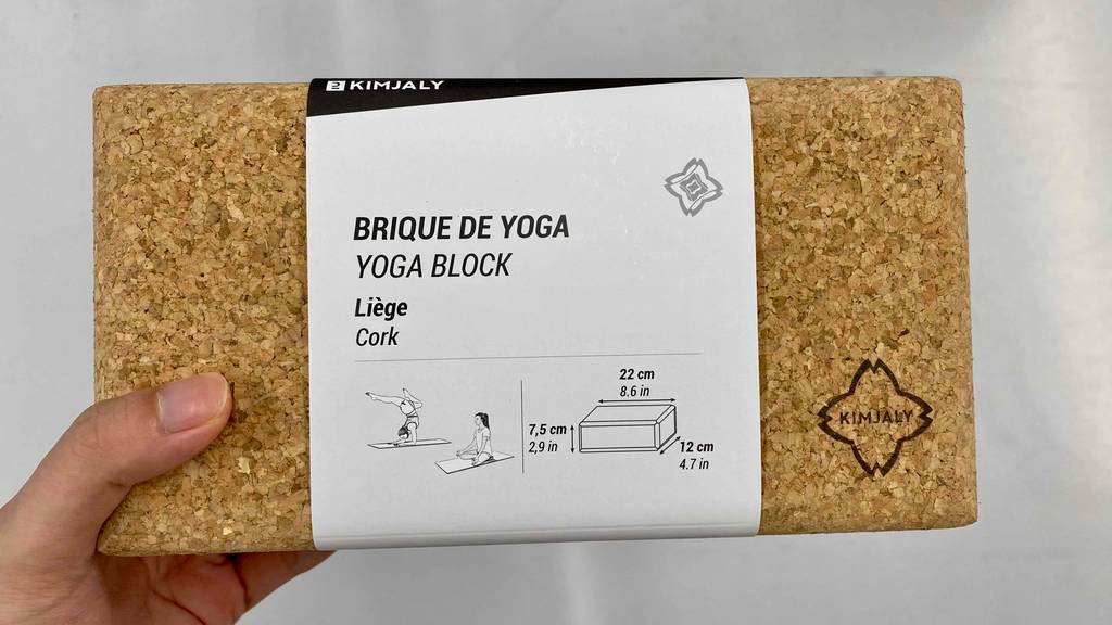 Eine Hand hält einen Yogablock vor einer weißen Wand.
