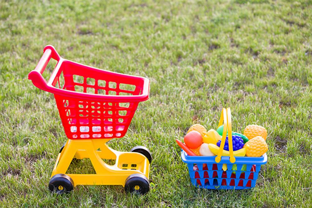 Kinder-Einkaufswagen im Test: Ein rot-gelber Kinder-Einkaufswagen mit einem blauen Korb, der mit Obst und Gemüse als Spielzeug gefüllt ist.