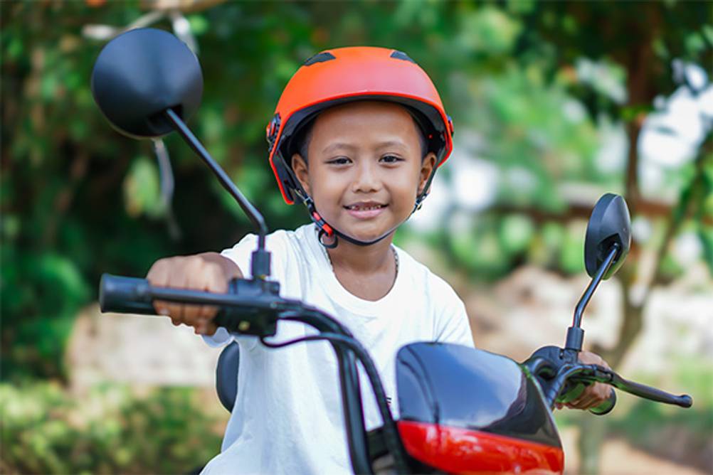 Kinder-Elektromotorrad im Test: Ein Junge mit orangenem Helm, der stolz sein Motorrad präsentiert.