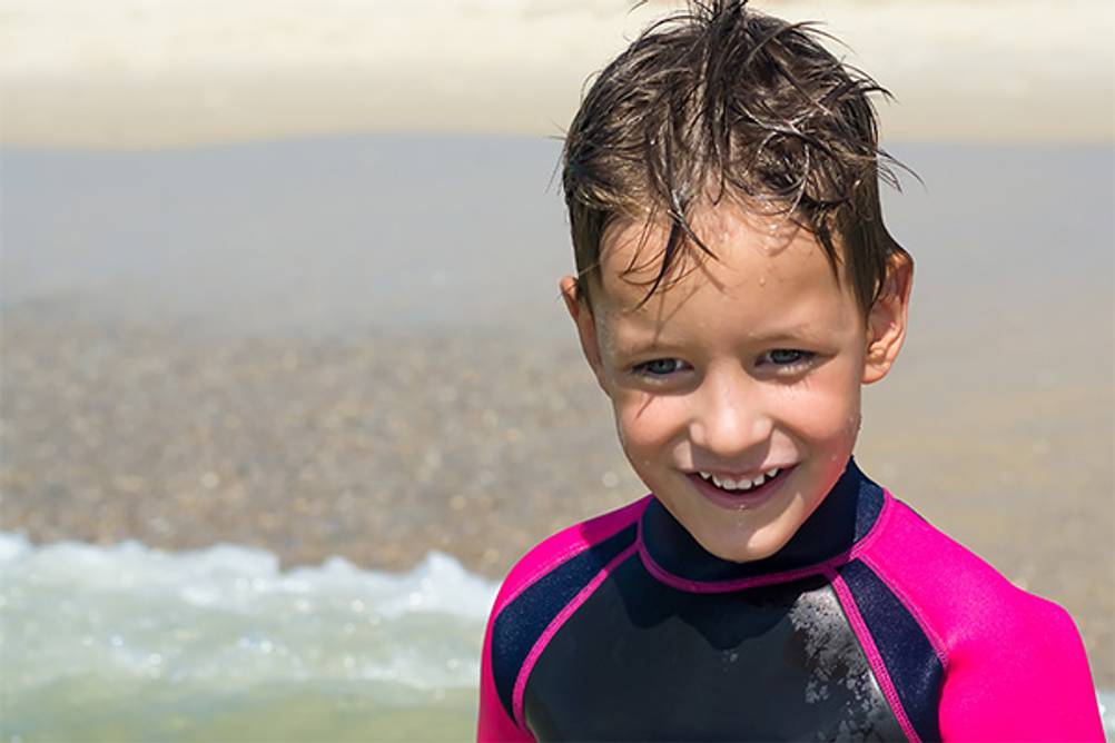 Kinder-Neoprenanzug im Test: Ein Junge im Wasser mit einem schwarz-pinken Neoprenanzug.