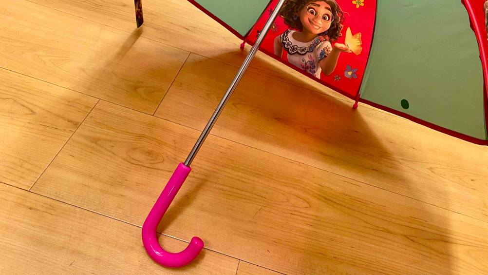 Nahaufnahme des Griffes eines geöffneten Kinder-Regenschirms im Test auf einem Holzboden.