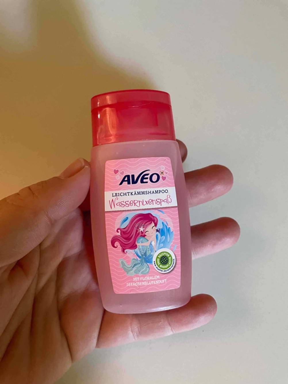 Eine Hand hält eine Flasche des getesteten Kinder-Shampoos vor eine hellen Wand.