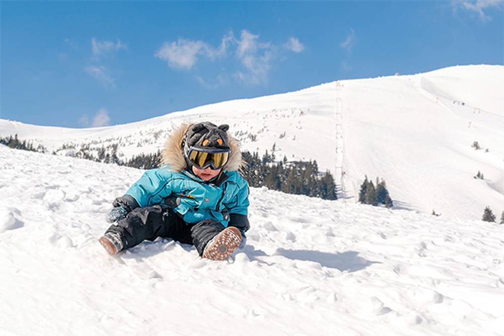 Kinder-Skibrillen im Test: Ein kleiner Junge, der im Schnee sitzt und eine Kinder-Skibrille trägt.