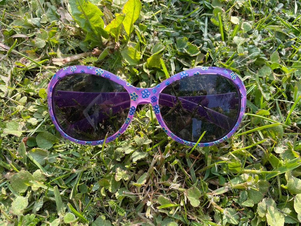 Kinder-Sonnenbrille getestet: Eine lila Sonnenbrille mit Blümchenmuster auf einer Wiese.