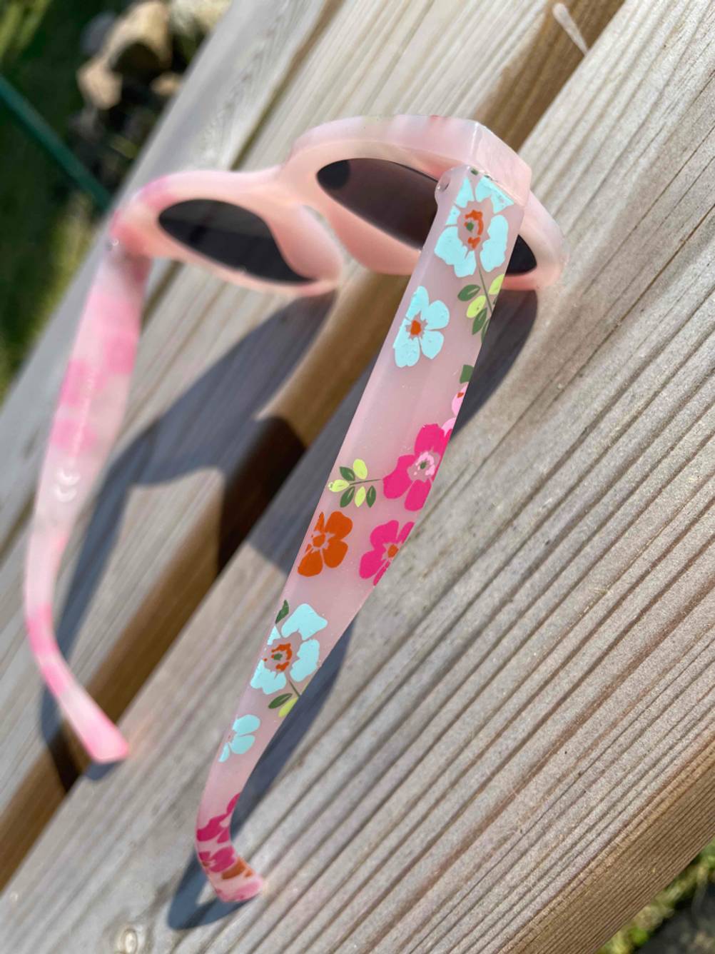 Nahaufnahme der Seitenbügel mit Blumen einer getesteten Kinder-Sonnenbrille auf einem Holztisch.