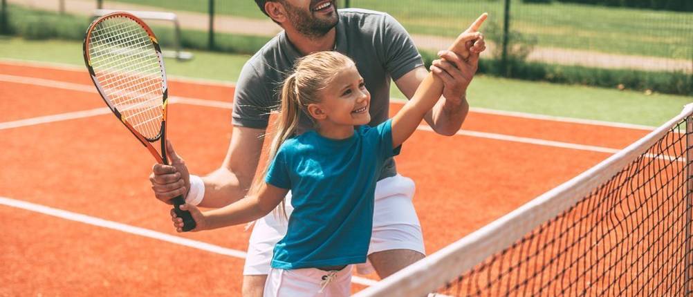 Ein Kind übt mit einem Trainer Tennis