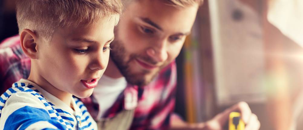 Kinder-Werkbank im Test: Hier ist ein Junge mit seinem Vater zu sehen, der ein Stück Holz vermisst.
