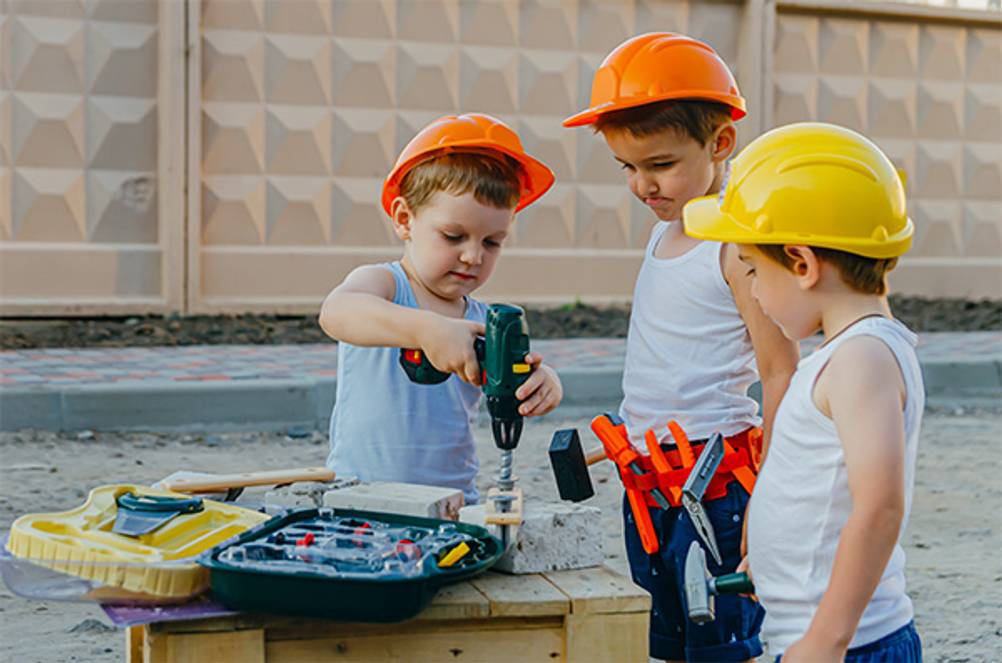 Kinder-Werkzeugkoffer im Test: Drei Jungs die gemeinsam an einem Bauprojekt arbeiten. Sie haben viel Werkzeug und Schutzhelme auf.