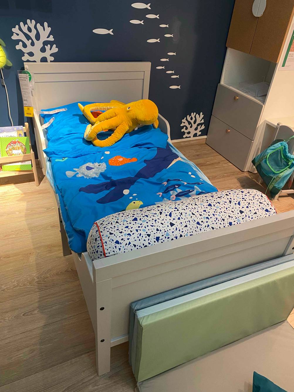 Ein graues Kinderbett mit blauer Bettdecke