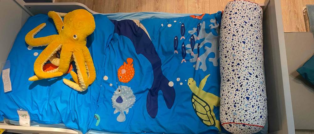 Ein graues Kinderbett mit blauer Bettdecke