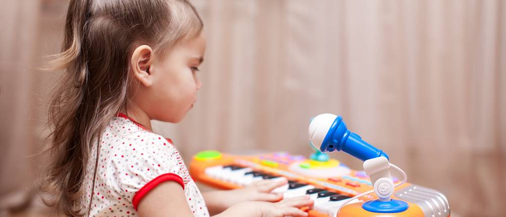 Child little girl playing on a toy piano at home