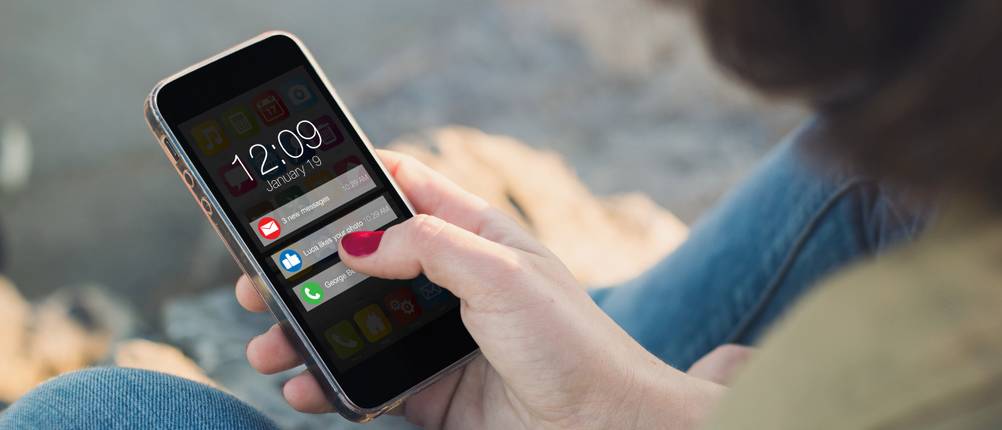 Eine Frau hält ein Smartphone in der Hand auf welchem verschiedene Push-Nachrichten zu sehen sind.