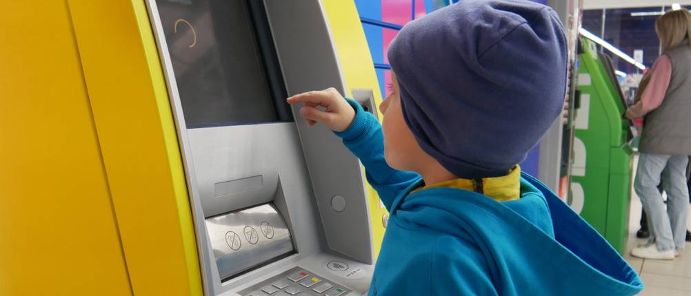 Ein Kind hebt an einem Bankautomat Geld ab.