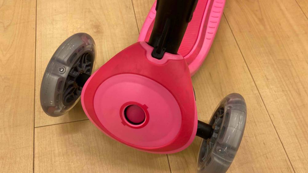 Nahaufnahme der Vorderräder eines getesteten Kinderrollers mit 3 Rädern auf einem Holzboden.