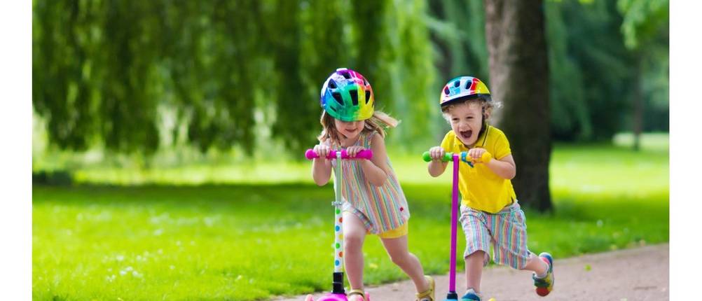 Kinderoller im Test: Zwei Kinder mit Helm fahren mit einem Kinderroller einen Weg entlang.
