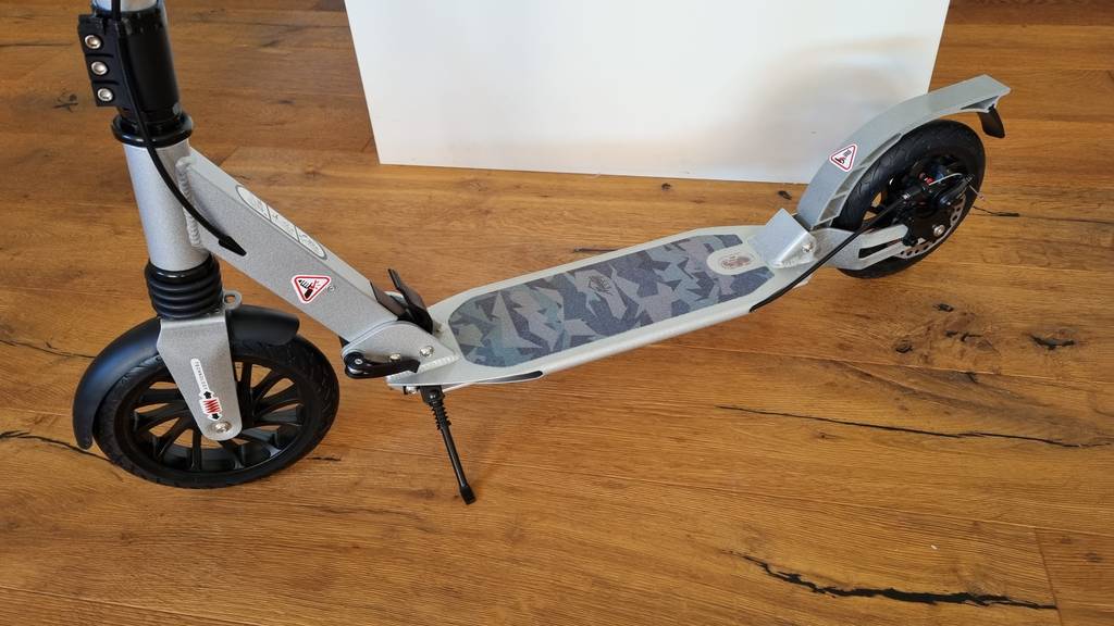 Grauer Kinderroller im Test mit Ständer auf einem Holzboden.