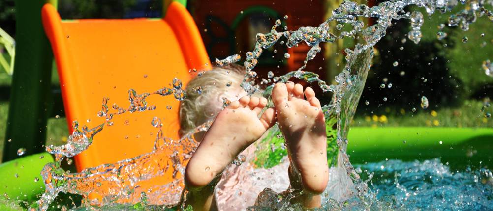 Kinderrutsche im Test: Eine orangene Rutsche, die in ein kleines Plantschbecken im Garten mündet.