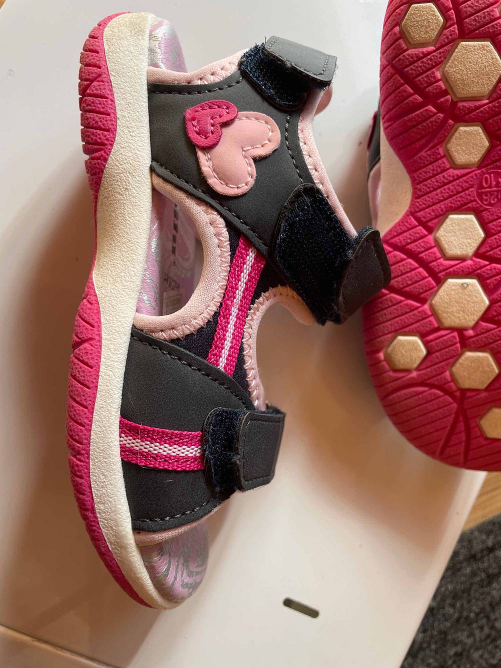 Im Test: Eine Kindersandale auf der Seite liegend, daneben ein Schuh mit der Sohle nach oben.