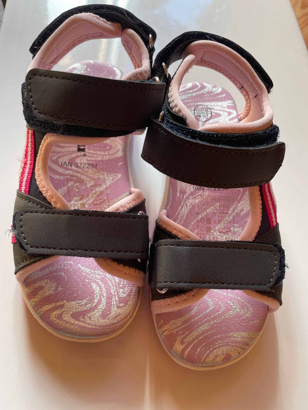 Ein Paar getestete Kindersandalen in schwarz-rosa nebeneinander von vorne.