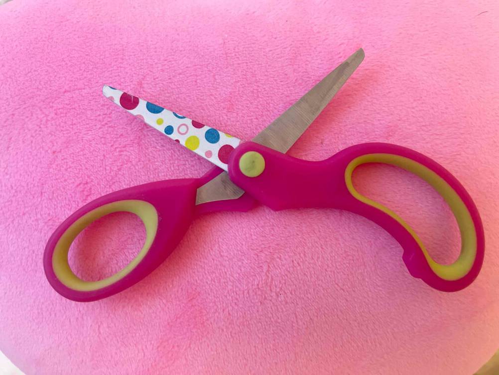 Auf einer pinken Fläche liegt eine geöffnete Kinderschere im Test.