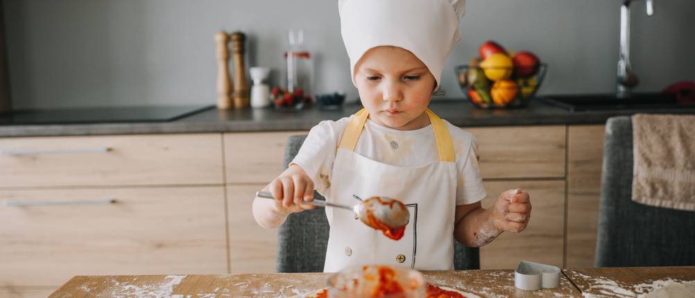 Kinderschürze-Test: Kind belegt Pizza mit Soße.
