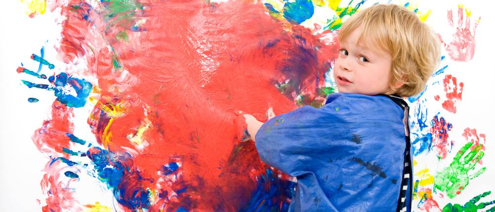 Kinderschürze-Test: Kind mit Malerkittel malt mit Fingerfarben.