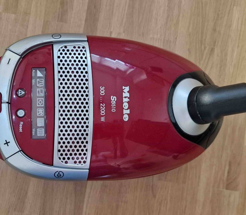 Ein roter Kinderstaubsauger im Test auf einem Holzfußboden, von oben betrachtet.