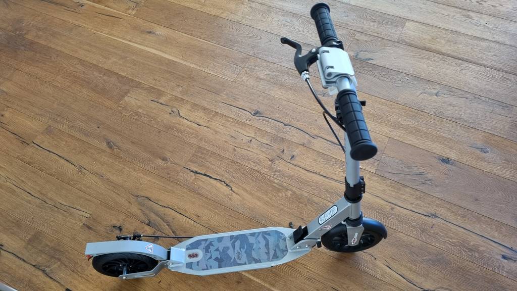 Grauer getesteter Kinderroller mit Handbremse auf einem Holzboden stehend.
